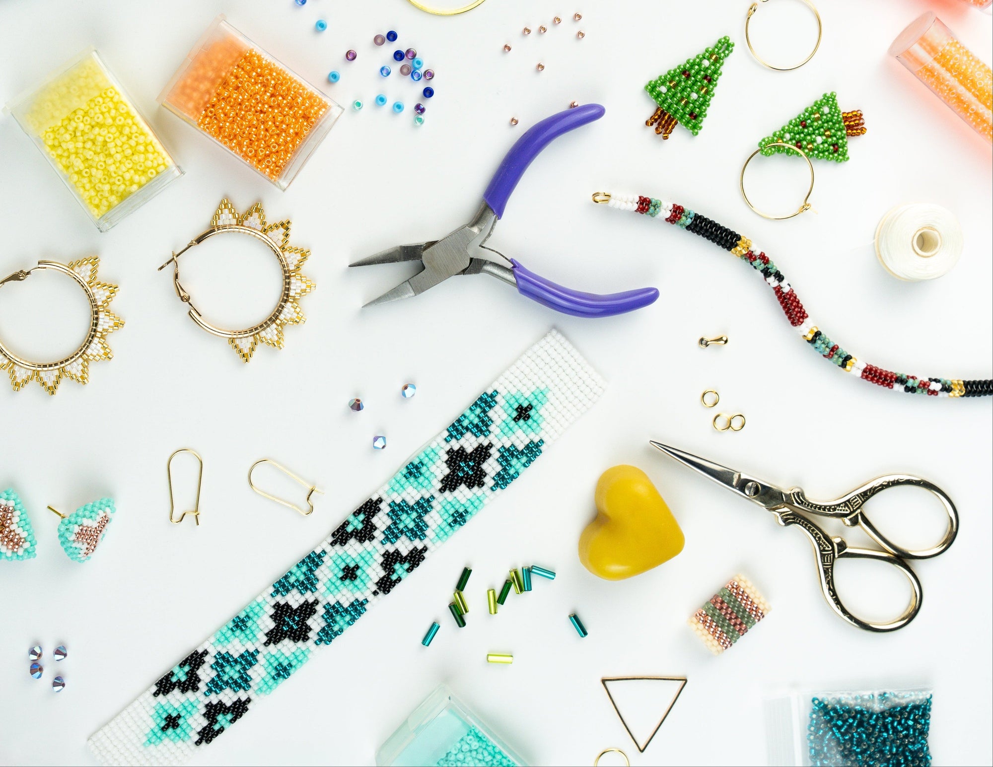 Jewelry-making supplies including beads, scissors, and pliers on a white surface.